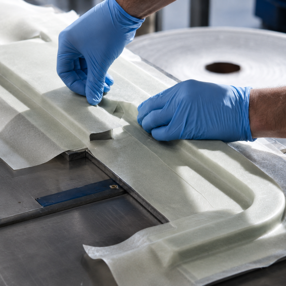Gloved hands placing composite fabric into a mold during layup