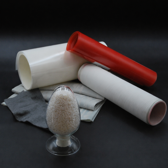 White and red film rolls, gray nonwoven fabric and a glass dish of polyester chips
