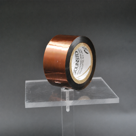 208X Pi Hi-Shrink Tape - an amber-brown roll of polyimide Hi-Shrink Tape on a clear display stand.